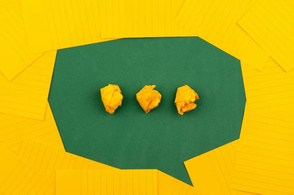 Yellow sticky notes forming a speech bubble on a green surface, with three paper balls—communication and taking a pause to respond.